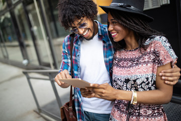 Attractive young african students are using a digital tablet and smiling while standing outside