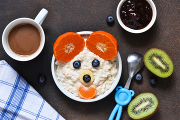 Fototapeta na wymiar Breakfast for child - cereal with fruits and berries. Cocoa beverage. The bear's face with a smile.