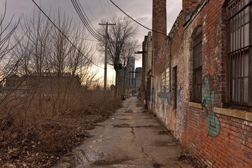 Industrial abandoned brick building in Detroit with grass growing through pavement and broken windows under cloudy gray sky