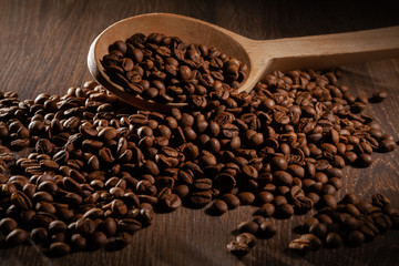  Scattered coffee beans with wooden spoons on wooden table.