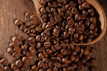  Scattered coffee beans with wooden spoons on wooden table.