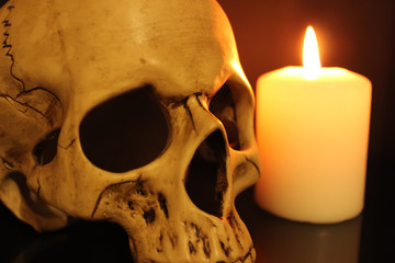 Human skull and white burning candle on black background