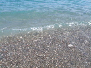 Sea wave runs on the beach covered with pebbles. Texture of clear turquoise water