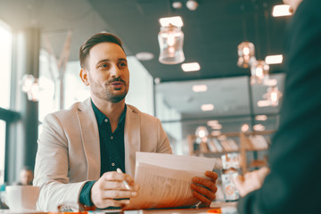 Positive handsome Caucasian unshaven businessman holding paperwork and talking to his colleague...