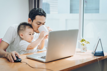 Asian little son helping father drinking coffee between working with laptop computer notebook at workplace happy family together at home concept.