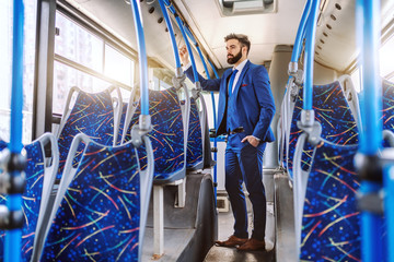 Full length of Caucasian bearded businessman in formal wear standing in public transportation and...