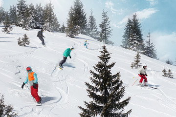Group of happy friends snowboarders and skiers riding on ski slope and having fun