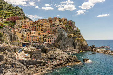 Fototapeta na wymiar Italy, Cinque Terre, Manarola, Cinque Terre, a group of people on a rocky beach with Cinque Terre in the background