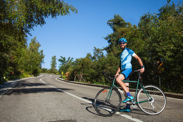 A man with a road bike in the mountains. Road serpentine to the mountains, surrounded by forest