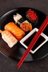 Concept of Asian cuisine. Japanese sushi with soy sauce on a black plate, on a black background. Red Chinese sticks. copy space