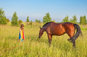 Little girl in  bright sundress and  horse in  grass on  meadow
