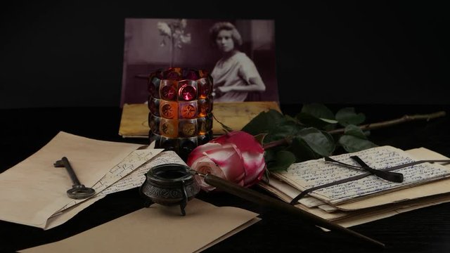 Burning candle in a glass candlestick and pink rose on the background of old letters, postcards and photographs. Family archive, memory