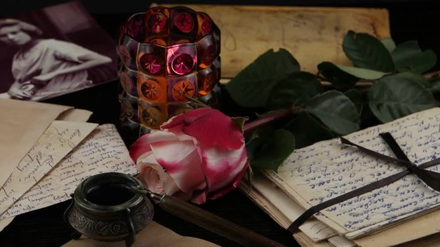 Still life with old letters, burning candle and rose on the black background. Family archive, memory