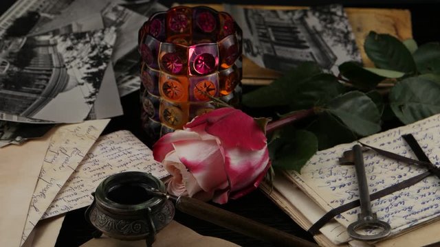 Burning candle in a glass candlestick and pink rose on the background of old letters and photographs. Family archive, memory