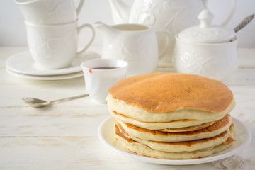 American pancakes with berry jam for breakfast and white dishes on a white wooden background with copy space