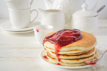 American pancakes with berry jam for breakfast and white dishes on a white wooden background with copy space