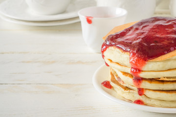 American pancakes with berry jam for breakfast and white dishes on a white wooden background with copy space