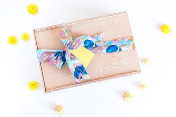 Wooden gift box with bow and yellow flowers on light background.