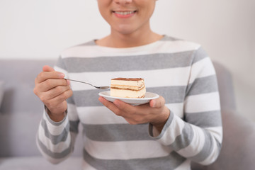 Young asian man eating cake while sitting on sofa at home.