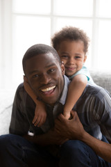 Portrait of smiling kid piggyback black young dad
