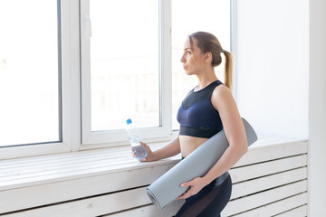 Fototapeta na wymiar Yoga, healthy and sport concept - Young fit woman holding grey mat and bottle of water