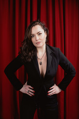 Fototapeta premium portrait of beautiful fancy stylish brunette woman with fashionable accessories in black suit on red curtains background