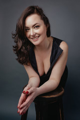 portrait of attractive, beautiful smiling brunette woman in suit with cleavage in studio on grey background