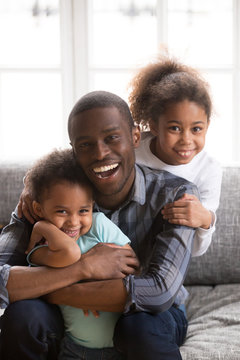 Portrait of happy black dad have fun hugging kids