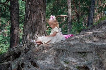 Little beautiful girl playing in nature in the forest. Sits on a bed under a pine tree