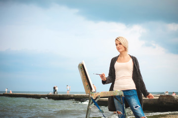 A young woman artist paints a landscape on the beach.