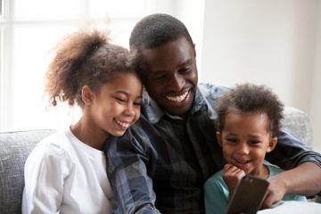 Happy black dad play on smartphone with little daughters