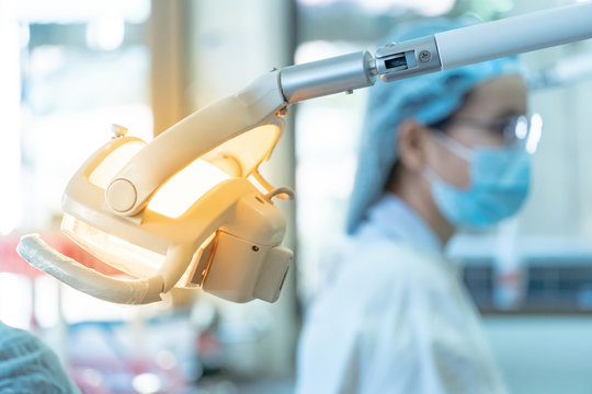 Close up of dental operatory light in dental clinic with blurred female Asian dentist in the background. Medical instrument concept