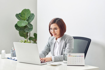 Beautiful business woman smile sitting at the desk working using laptop looking at screen typing on laptop over white background