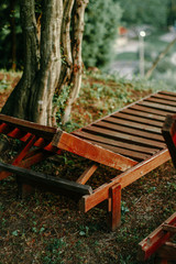old wooden chaise longue stands under a tree in the park