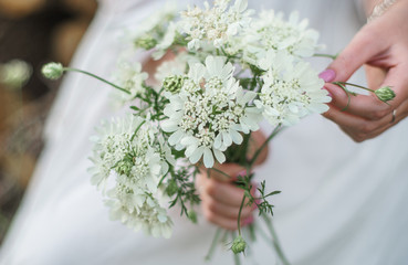 A girl in a white dress holds white flowers in her hands. Close shot.