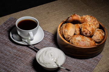 Pies in a wooden plate, a cup with a hot drink and a plate with sour cream stand on a table covered with a linen tablecloth.