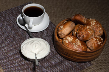 Pies in a wooden plate, a cup with a hot drink and a plate with sour cream stand on a table covered with a linen tablecloth.