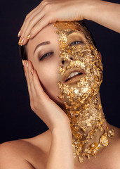 Closeup portrait of beautiful young woman with golden foil on face. Creative makeup.