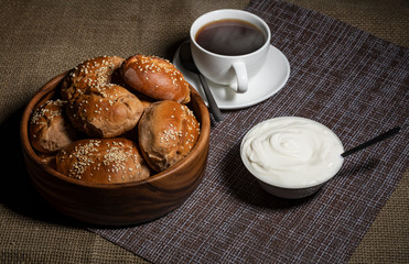 Pies in a wooden plate, a cup with a hot drink and a plate with sour cream stand on a table covered with a linen tablecloth.