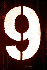 Number 9 in stencil on metal wall in orange tone.