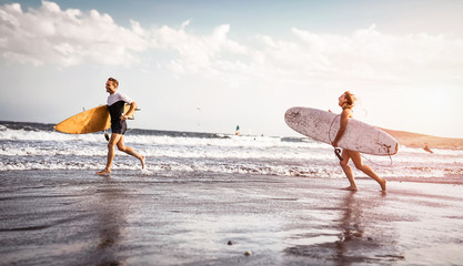 Happy surfers running with surfboards along the sea shore - Sporty couple having fun going to surf...