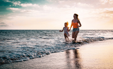 Mother and daughter running along the seashore at sunset - Happy family having fun playing together...