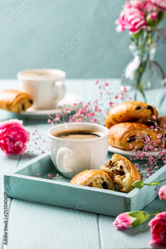 Holiday break with cup of coffee, mini fresh croissants chocolate bun and carnation flowers on turquoise background. Copy space.