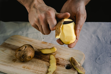 The chef cleans potatoes. For dishes with potatoes. On a black background, the concept of the menu,...