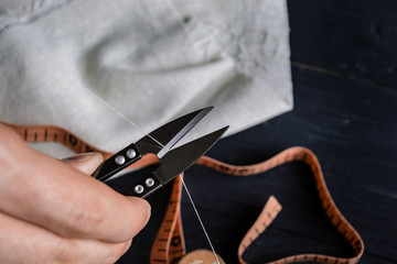 Obraz na płótnie Canvas Tailor cutting a thread with scissors, close up, black background
