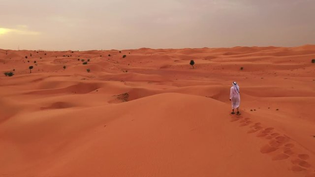 Desert sand dunes with man in typical Arabian suit walking.