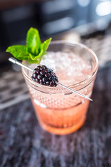 Cocktail drink bramble with black berries and mint at barcounter in night club or restaurant