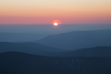 sunrise in the Carpathians on the background of blue mountain ranges and solar disk on the horizon. 