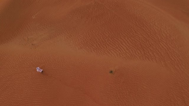 Desert sand dunes with man in typical Arabian suit walking.