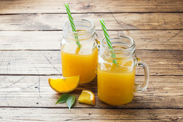 Orange juice in glass jars and fresh oranges on a wooden rustic background. Copy space.